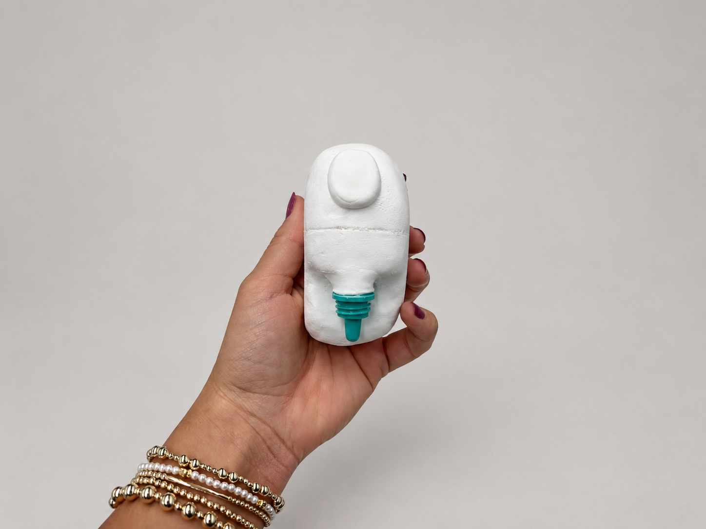 Hand holding a white foam appearance model of the accessible eyedrop dispenser against a neutral background