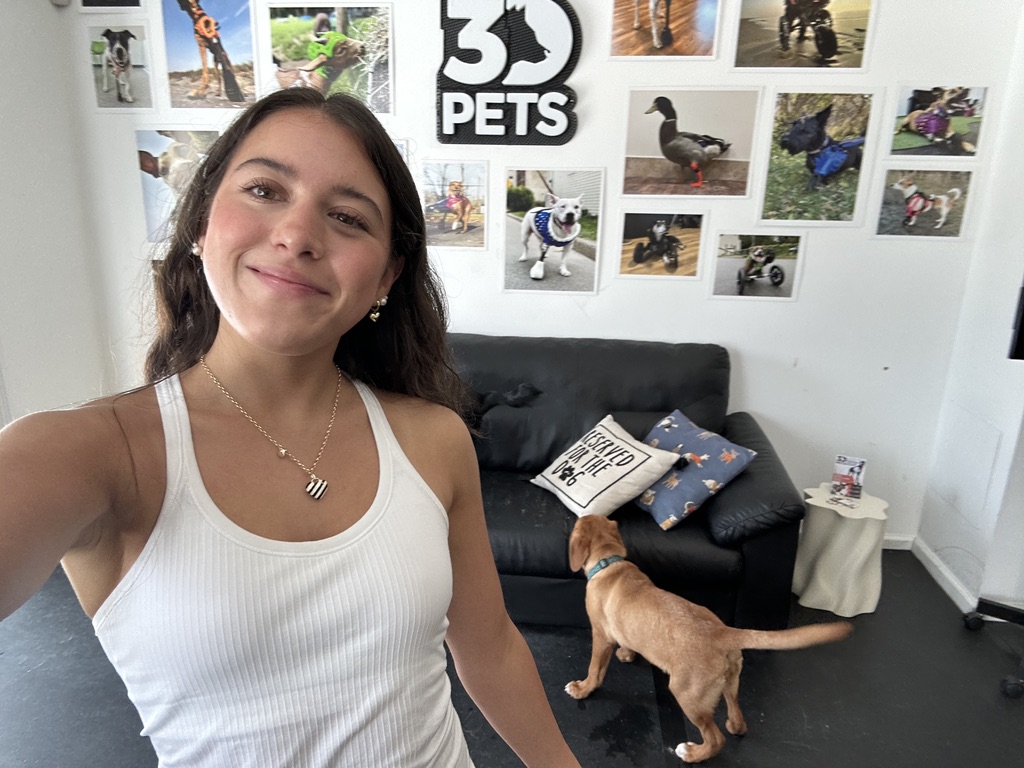 Lillian at the 3DPets studio surrounded by photos of animals using mobility devices